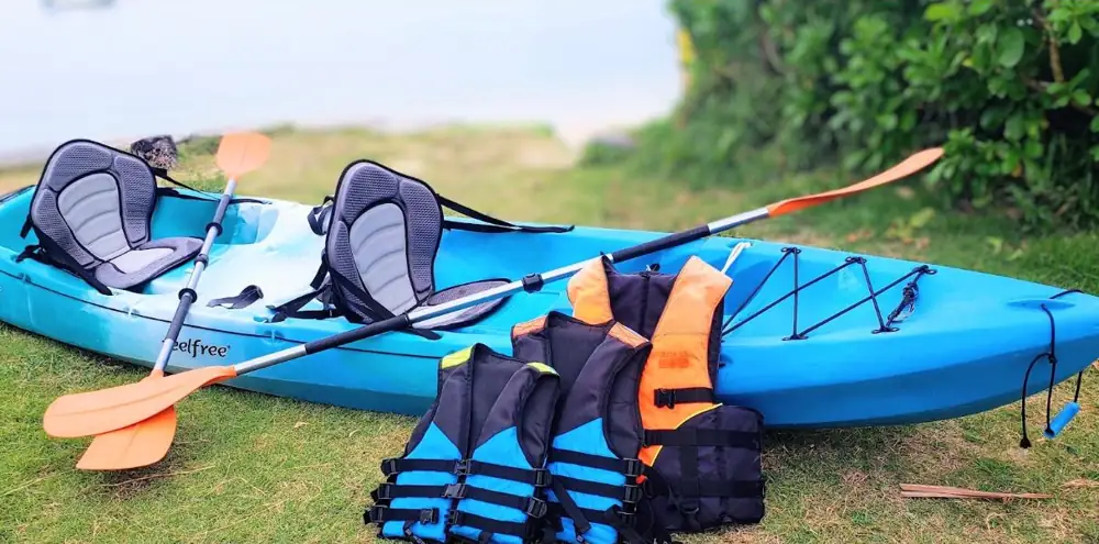 Two-seat kayak with paddles and life jackets on the grass by the beach